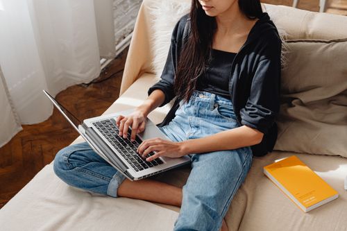 Free Young woman working on a laptop sitting comfortably on a sofa with natural light. Stock Photo