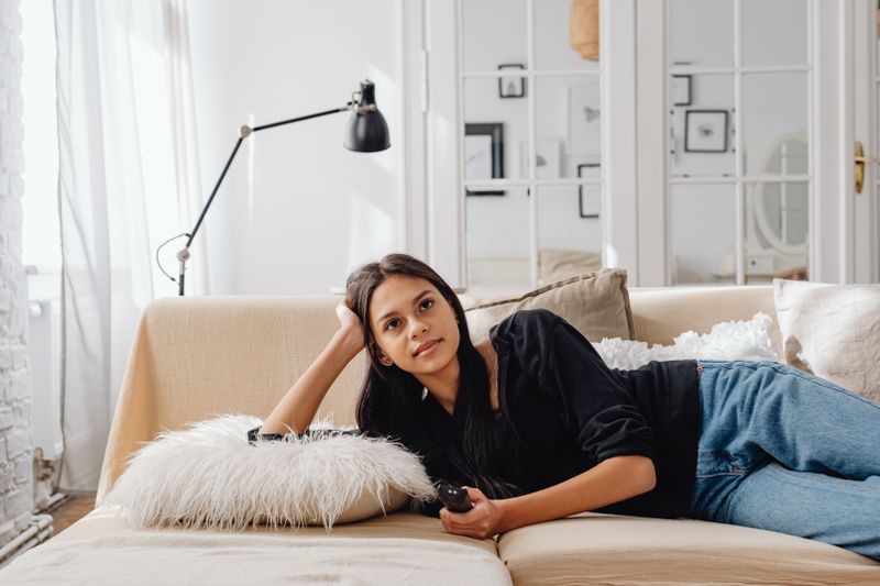 Woman lounging comfortably on a sofa with a remote control, enjoying leisure time indoors.