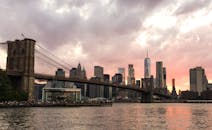 布鲁克林大桥和纽约市的天际线在日落时分映照在水面上，云层显得格外戏剧性