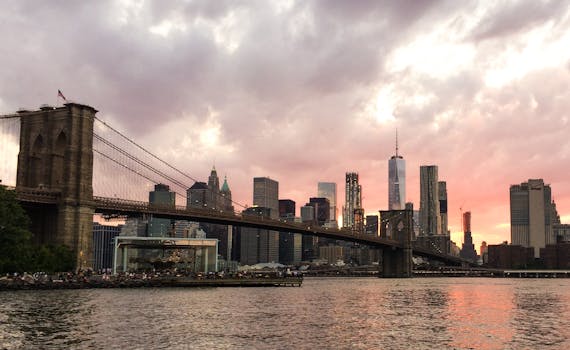 布鲁克林大桥和纽约市的天际线在日落时分映照在水面上，云层显得格外戏剧性