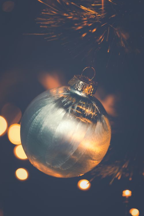 Free Close-up of a shimmering silver Christmas ornament hanging on a tree branch with festive bokeh lights. Stock Photo