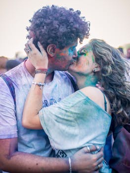 A vibrant couple embraces and kisses during a colorful Holi festival celebration.