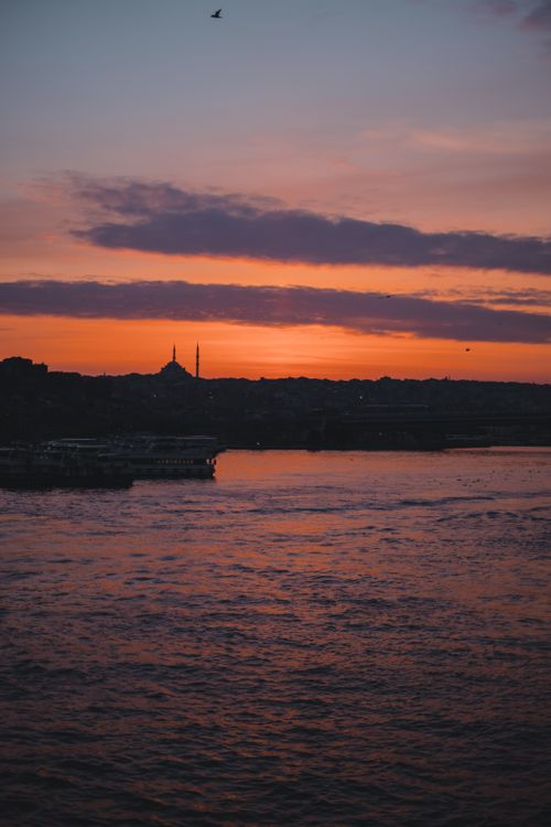 Free Rippled sea near coast with buildings in coastal town against colorful sky with clouds at sundown time on summer evening Stock Photo