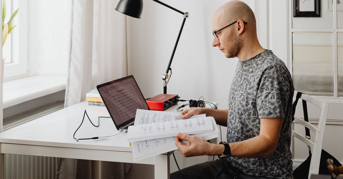 A young person sitting alone in a room, looking at a laptop with a thoughtful expression, surrounded by notes and a Bible