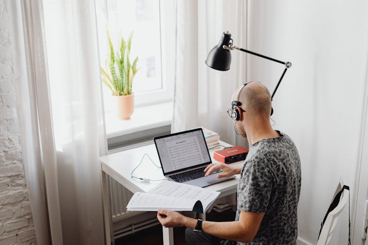 A Man In Printed Shirt Wearing Headset While Using His Laptop