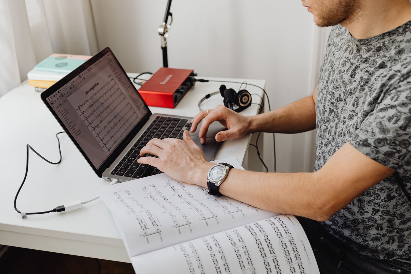 Musician working with a laptop and sheet music while preparing digital assets for fan communication