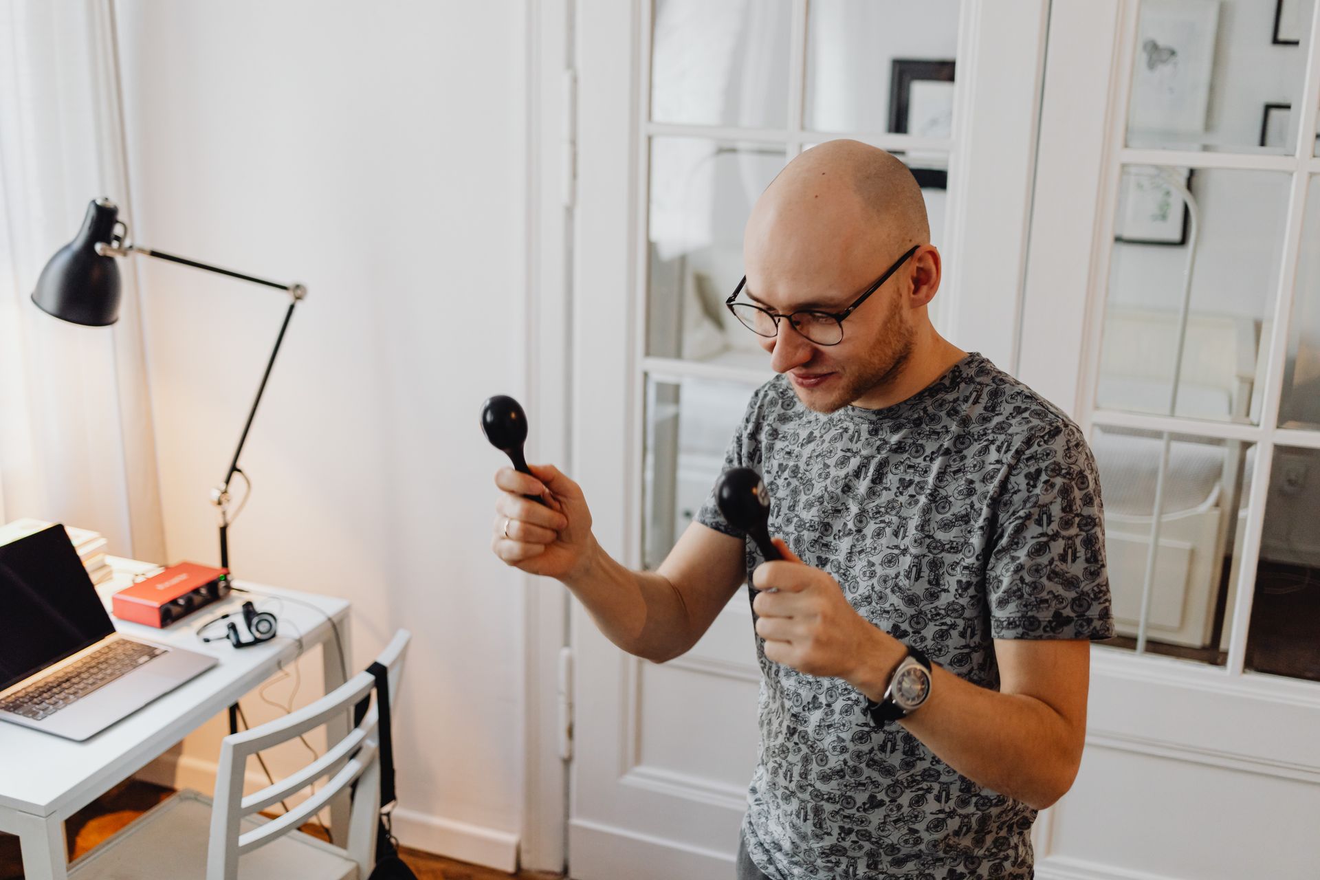 Bald man enjoying music with maracas in an office setting, showcasing casual creativity.