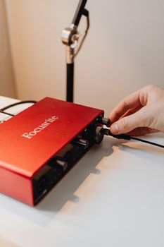 Hand adjusting settings on a red audio interface, ideal for musicians and podcasters.