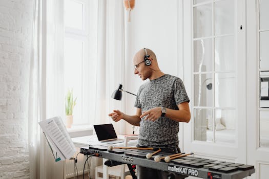 Musician wearing headphones playing mallet percussion with sheet music in bright room.