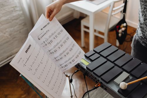 Free A musician's hand turns sheet music beside an electronic percussion instrument in a cozy room. Stock Photo