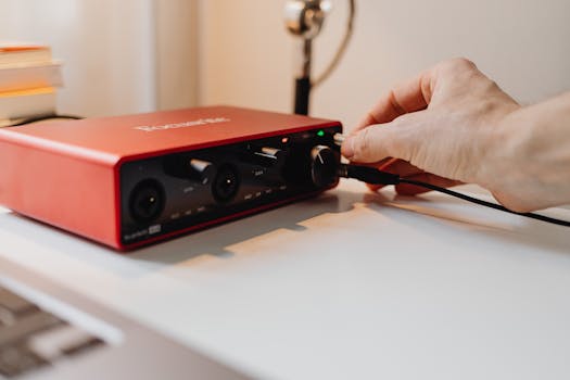 A close-up of a hand adjusting controls on a red audio interface, emphasizing technology use.
