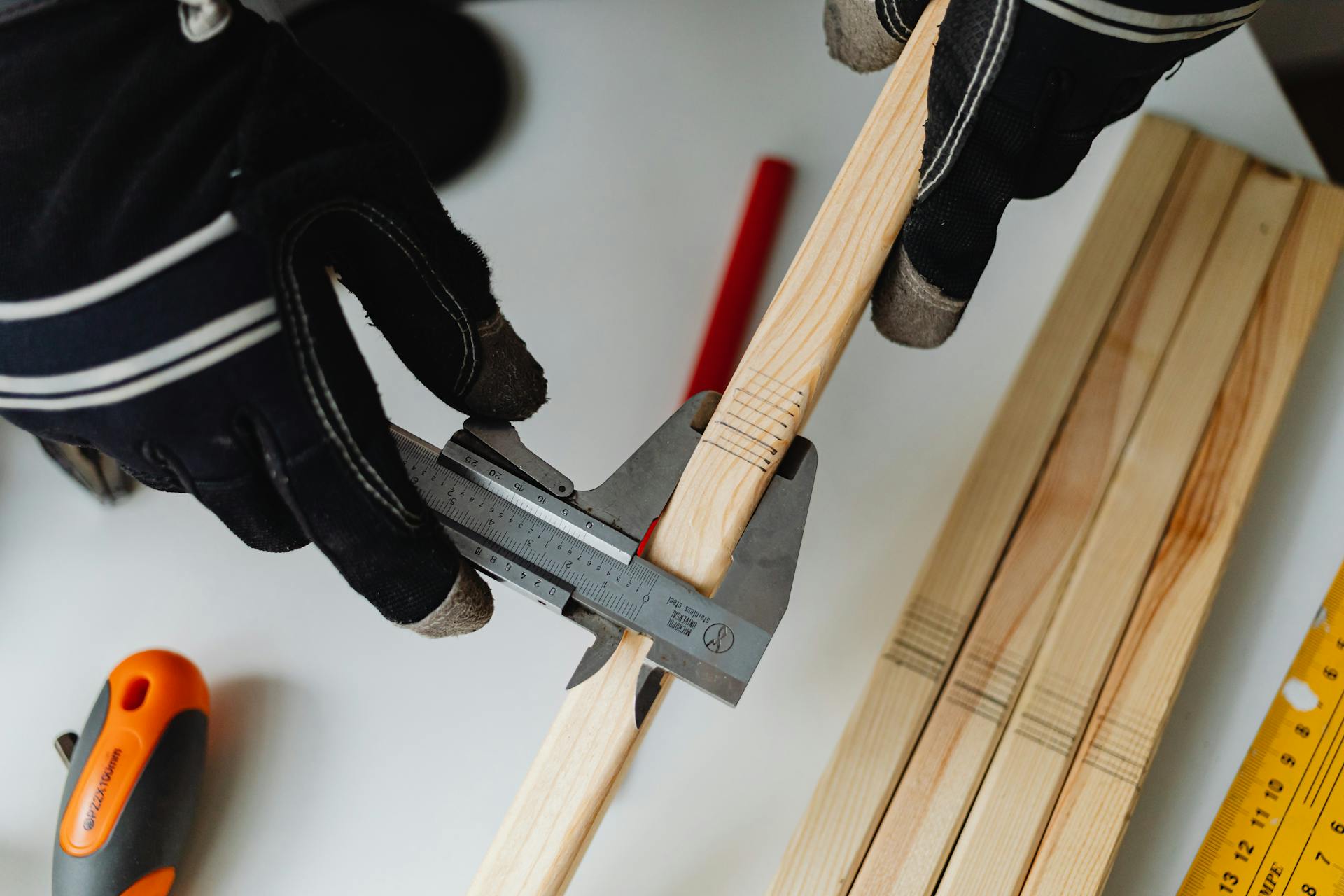 Close-up of hands measuring a wooden dowel with a caliper, showcasing precision and craft.