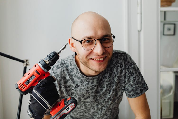 Portrait Of A Man Smiling Towards Camera With A Drill In Hand