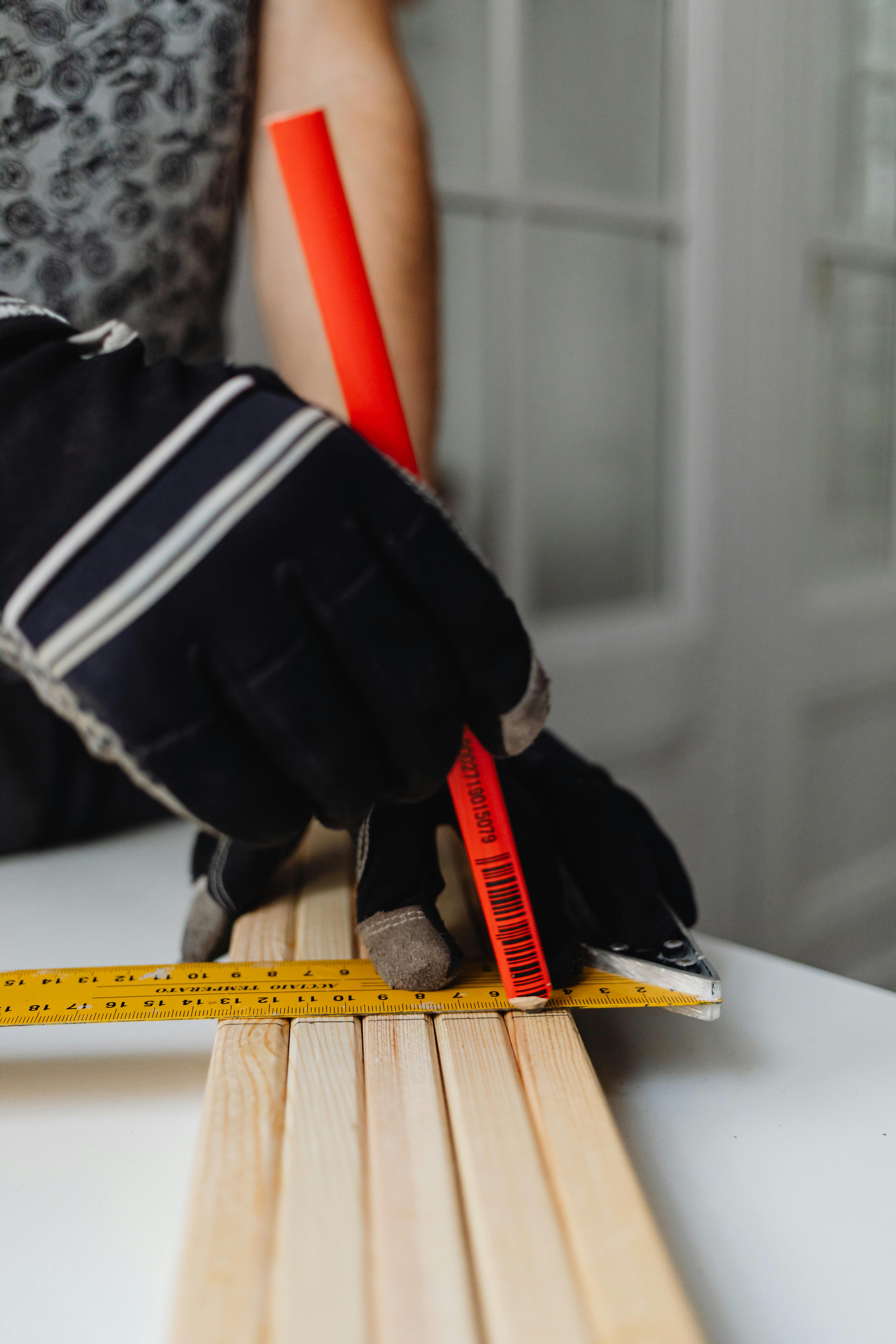 Close-up of a craftsman measuring wood with tape and marker in a workshop.