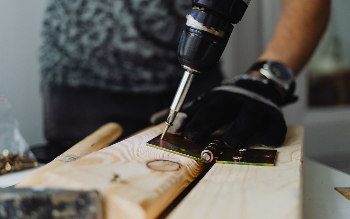 Close-up of a handyman’s hands using a drill on a wooden plank during a home repair
