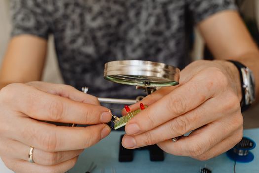 Close-up view of a person fixing an electronic circuit board with a magnifier.