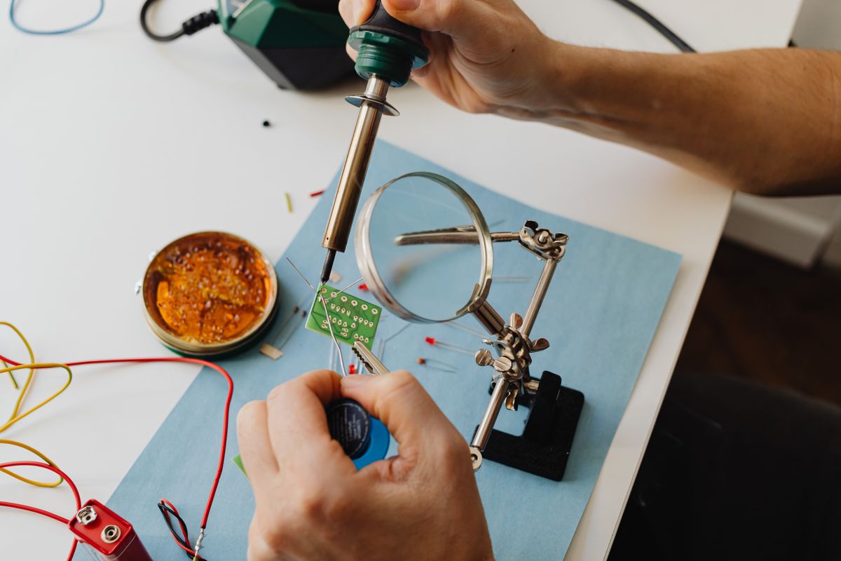 Technician soldering a circuit board under a magnifying glass