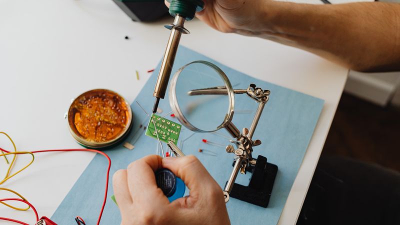 hobbyist soldering power electronics on a workbench with a multimeter and oscilloscope nearby