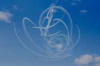 From below of air tattoo with airplanes demonstrating acrobatic flight with wavy traces in cloudy sky