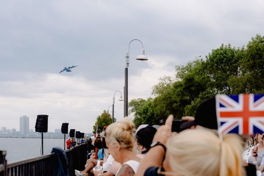 Crop anonymous people with UK flag admiring plane flying in cloudy sky during festive event in town