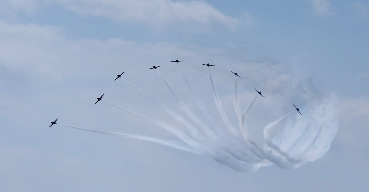 Low angle of airplanes in row performing air tattoo with wavy traces in cloudy sky in daytime