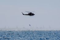 Copter landing anonymous military parachutist over wavy ocean with sailboats during professional practice in daytime