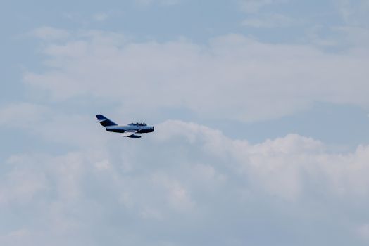 Creative design of modern fighter aircraft flying in light sky with fluffy clouds in daylight