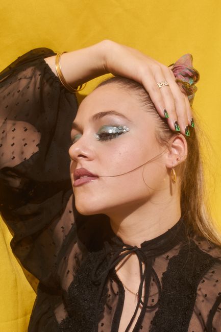 Fashionable portrait of a woman posing with pearl makeup against a yellow background.