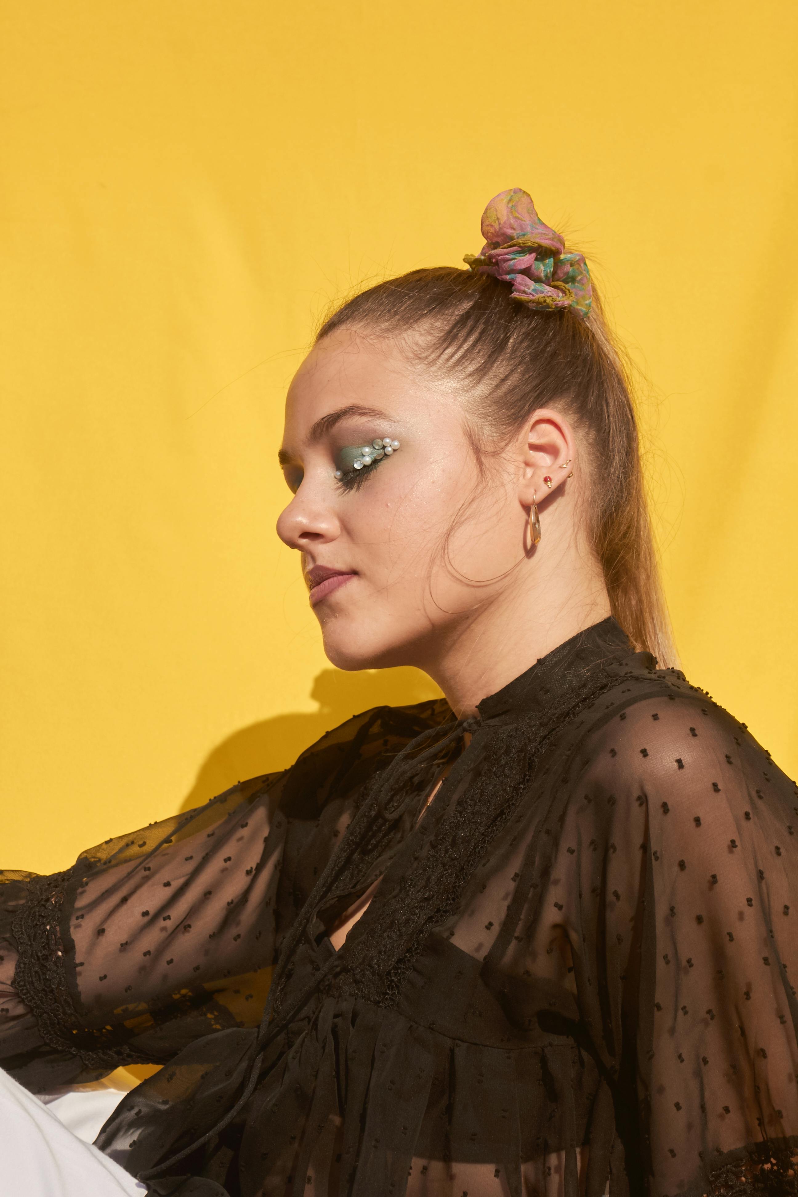 Stylish portrait of a woman in a sheer black blouse against a vibrant yellow background.