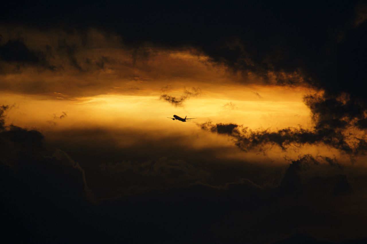 a striking silhouette of an airplane flying through a moody golden sky