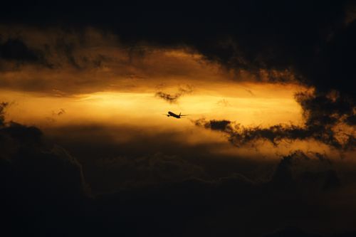 Free A striking silhouette of an airplane flying through a moody, golden sky during sunset. Stock Photo