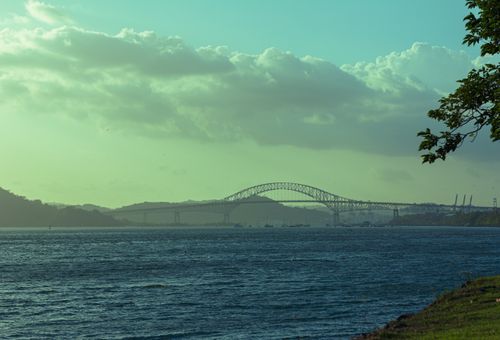 Free A stunning twilight view of a suspension bridge over a calm river with scenic clouds and horizon. Stock Photo