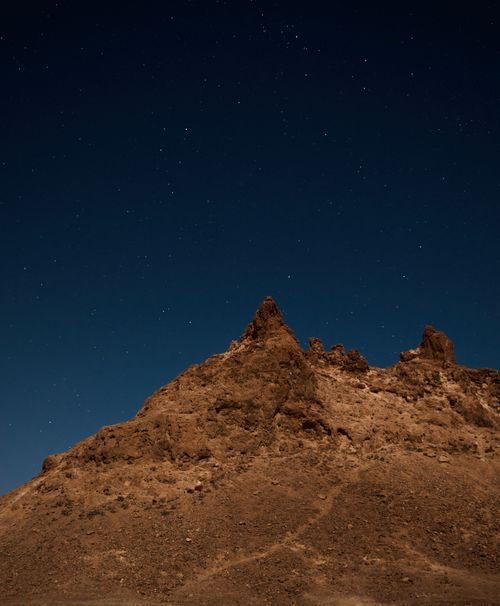 Free A serene desert mountain under a starry night sky, showcasing natural geological formations. Stock Photo