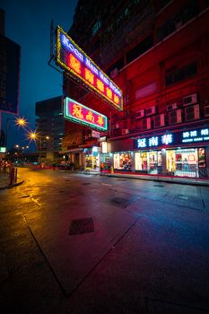Hong Kong street illuminated by vibrant neon signs, reflecting on wet roads at night.