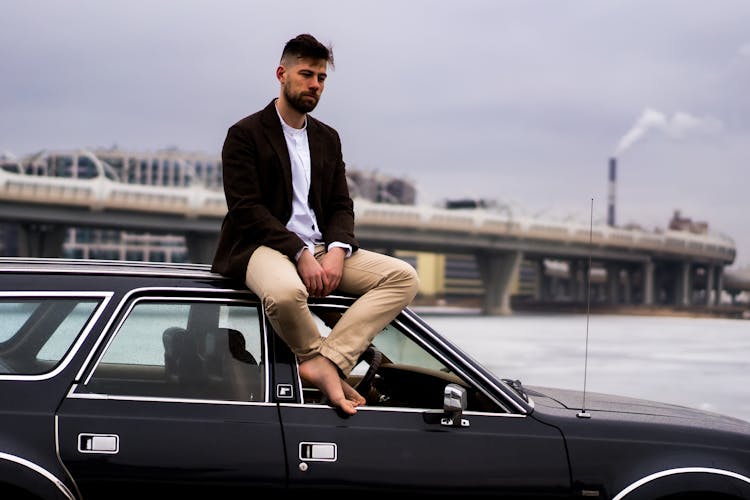 A Bearded Man Sitting On The Roof Of A Car