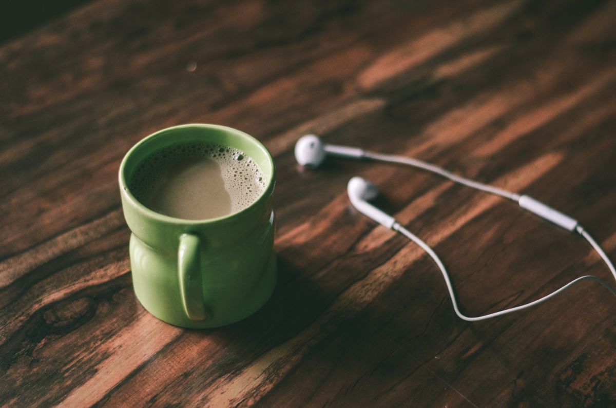 A green mug of coffee beside a pair of earphones on a wooden table