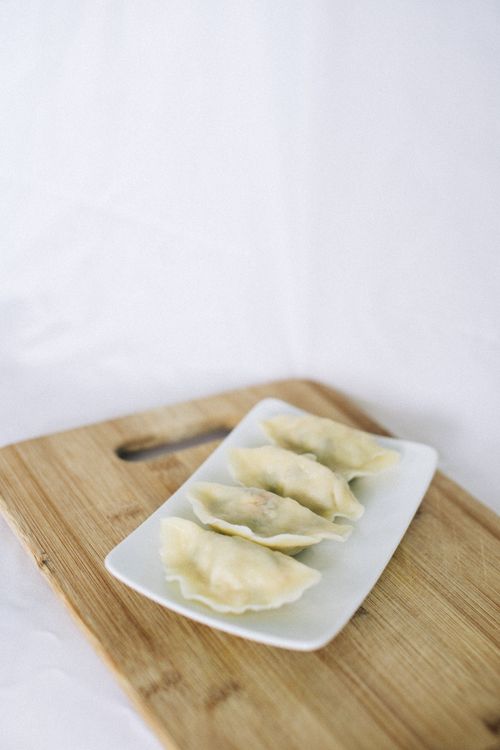 Free A minimalist close-up of four dumplings on a white plate with a wooden board background. Stock Photo