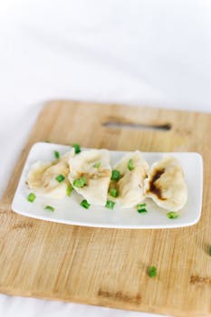 Four steamed dumplings garnished with green onions on a wooden board, showcasing Asian cuisine.