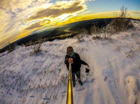 Person takes a selfie on a snowy mountain at sunset, capturing a scenic winter landscape.
