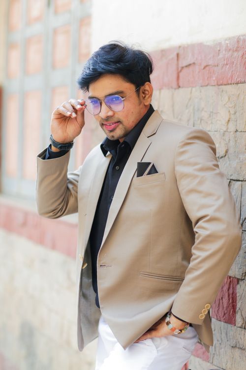 Free Fashionable man posing confidently outdoors in a sleek beige blazer and sunglasses. Stock Photo