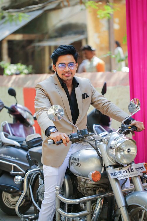 Free A fashionable man in a beige suit confidently poses on a motorcycle outdoors in Mumbai. Stock Photo