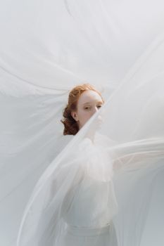 Dreamlike portrait of a redheaded bride enveloped in a flowing white veil, exuding elegance.