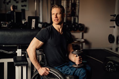 A Man Sitting on a Wheelchair while Holding a Dumbbell