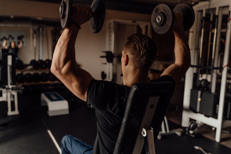 Man In Black Shirt Sitting On A Wheelchair While Holding Dumbbells