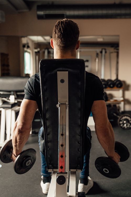 Free A muscular man performing a dumbbell exercise in a fitness center, showcasing strength and focus. Stock Photo