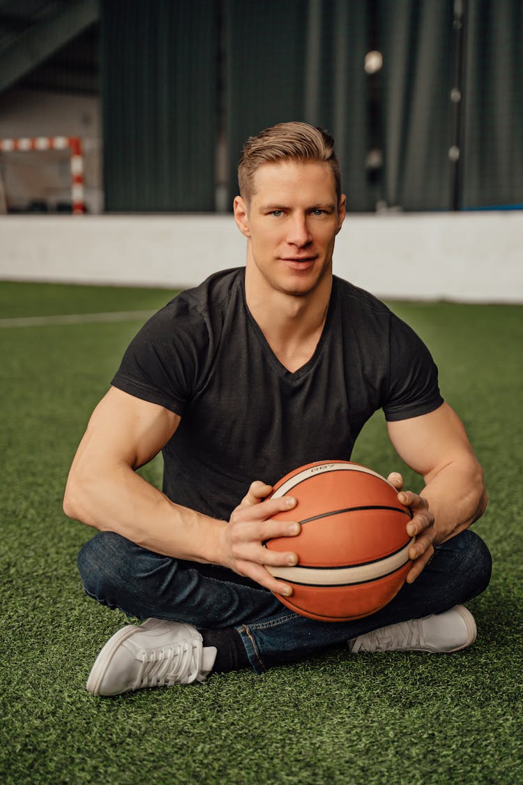 Man Sitting On Grass Field Holding A Ball