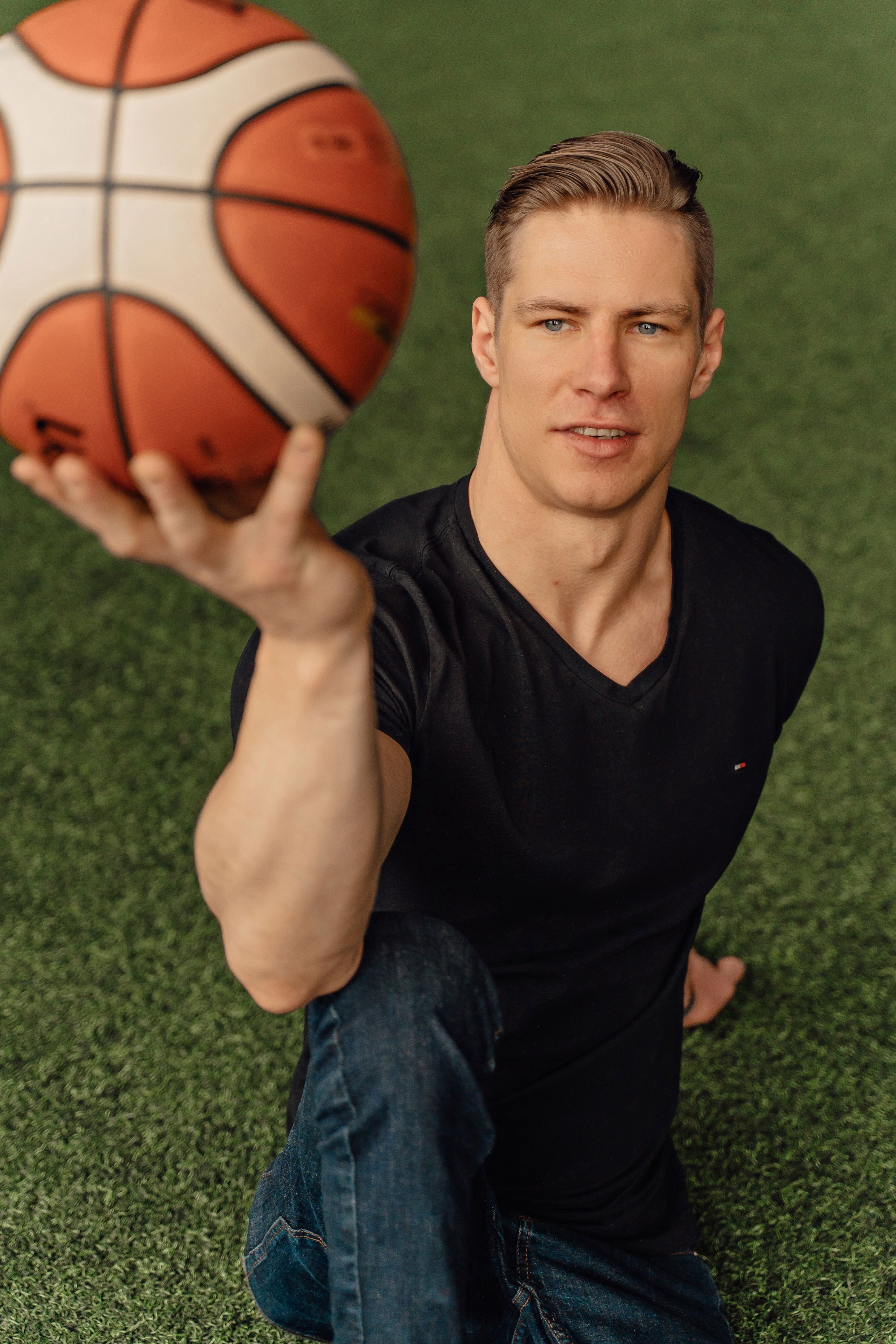 Athletic man in a black shirt skillfully balances a basketball on a green grass field.