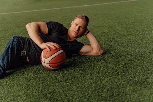 Athletic man lying on a grassy field holding a basketball, captured outdoors.