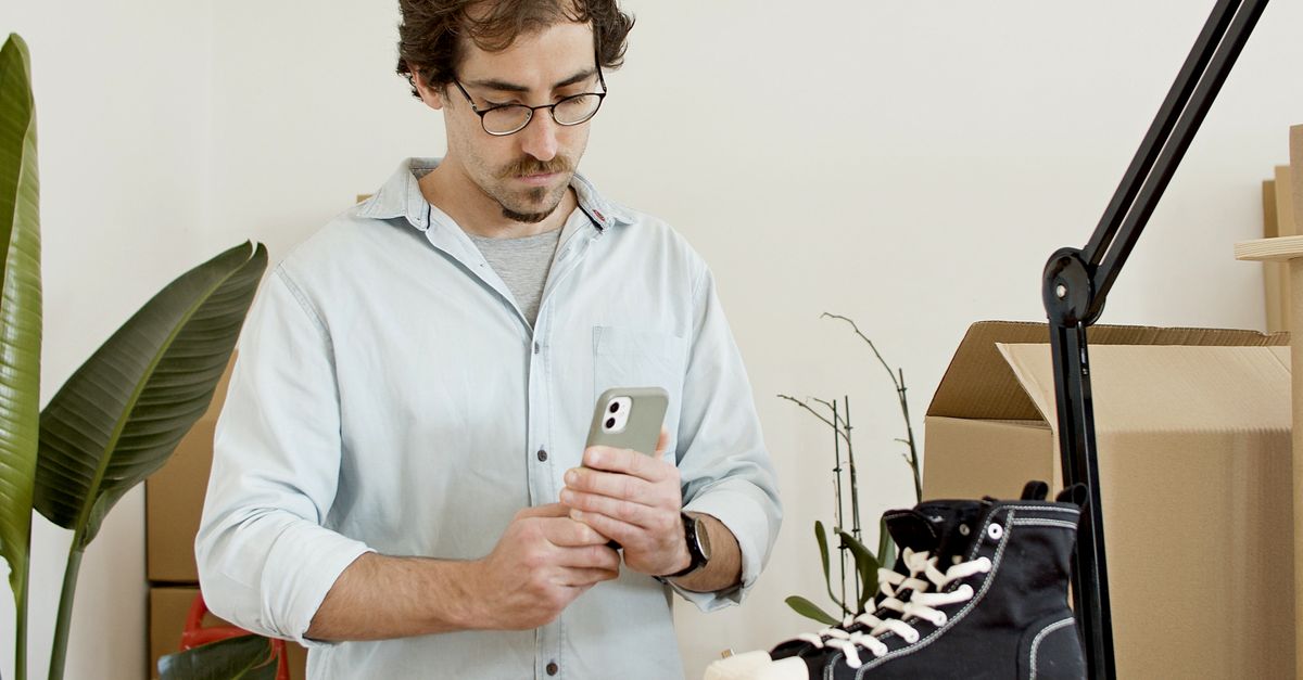 Man uses phone to photograph sneakers in an indoor business setup with boxes.