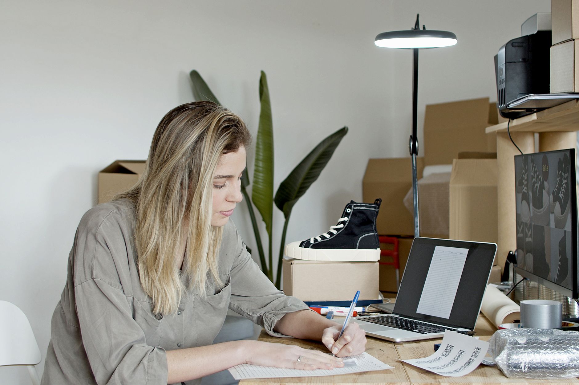 Businesswoman writing notes in a busy online store office in Portugal, focusing on growth and efficiency.